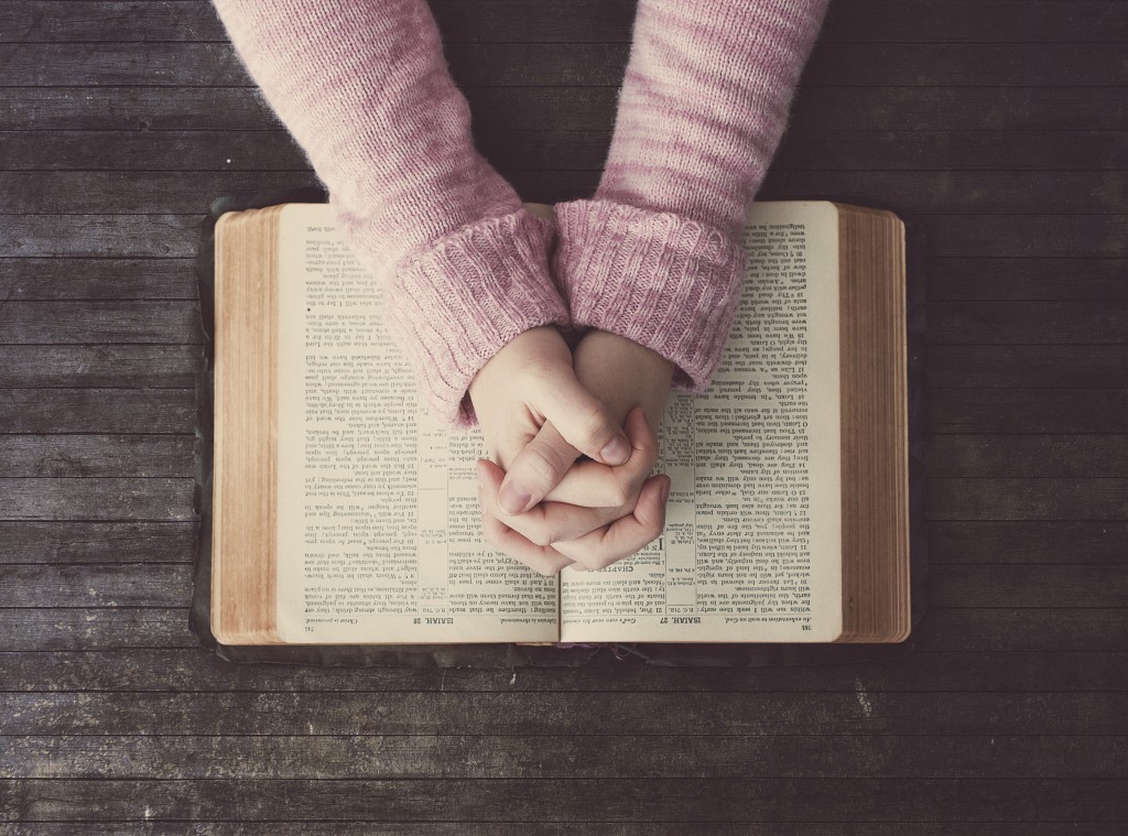 Woman praying over a Bible on a wooden table.